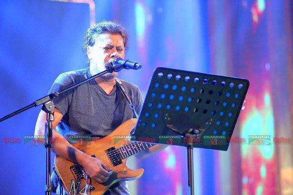 গায়ক গিটার বাজিয়ে পারফর্ম করছেন, মঞ্চে আলো ও ব্যাকগ্রাউন্ড লাইট. Channel i News - চ্যানেল আই নিউজ
