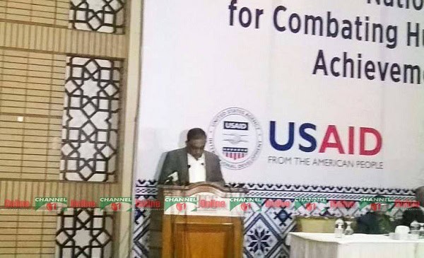 স্বরাষ্ট্রমন্ত্রী বক্তব্য দিচ্ছেন, পেছনে USAID লোগো দেখা যাচ্ছে. Channel i News - চ্যানেল আই নিউজ