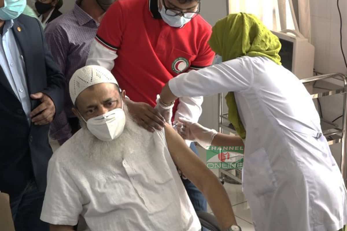 বাংলাদেশের একজন ব্যক্তি করোনাভাইরাসের টিকা নিচ্ছেন, স্বাস্থ্যকর্মী সহায়তা করছেন. Channel i News - চ্যানেল আই নিউজ