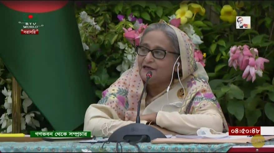 বাংলাদেশের একজন নারী বক্তা মঞ্চে বক্তৃতা দিচ্ছেন, ফুলের পেছনে।. Channel i News - চ্যানেল আই নিউজ