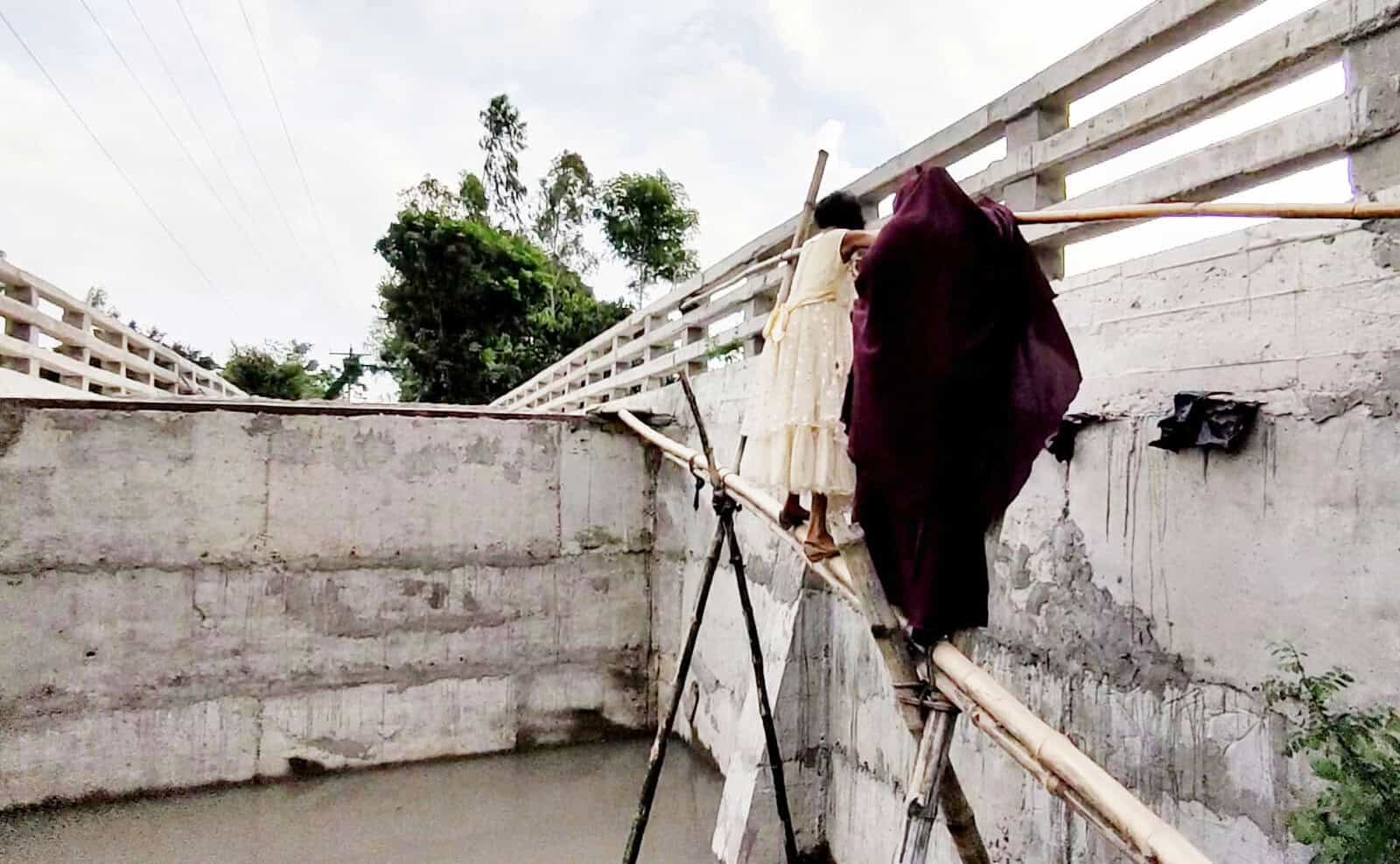 বাঁশের খুঁটির সাহায্যে কালভার্টে উঠছে একজন শ্রমিক. Channel i News - চ্যানেল আই নিউজ