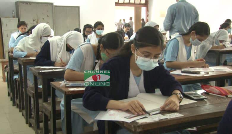 Students taking exam in classroom, wearing masks, focused on papers. Channel i News - চ্যানেল আই নিউজ