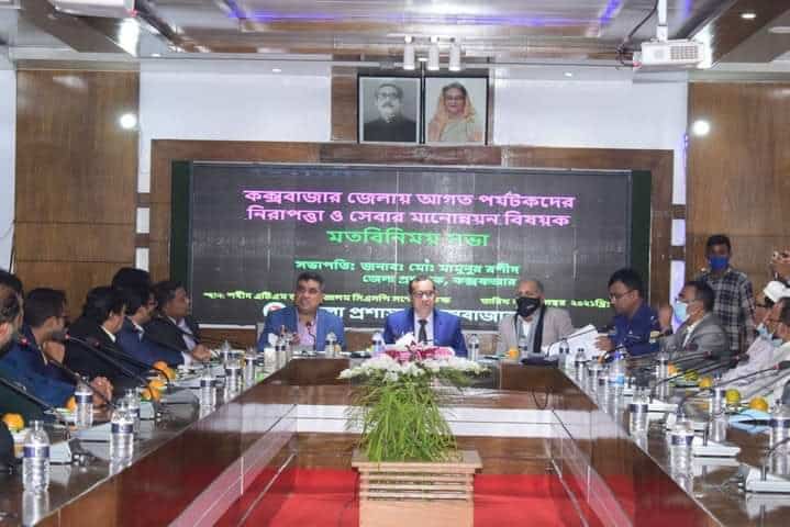 সভা চলাকালে আলোচক ও উপস্থিত ব্যক্তিরা বসে আছেন. Channel i News - চ্যানেল আই নিউজ