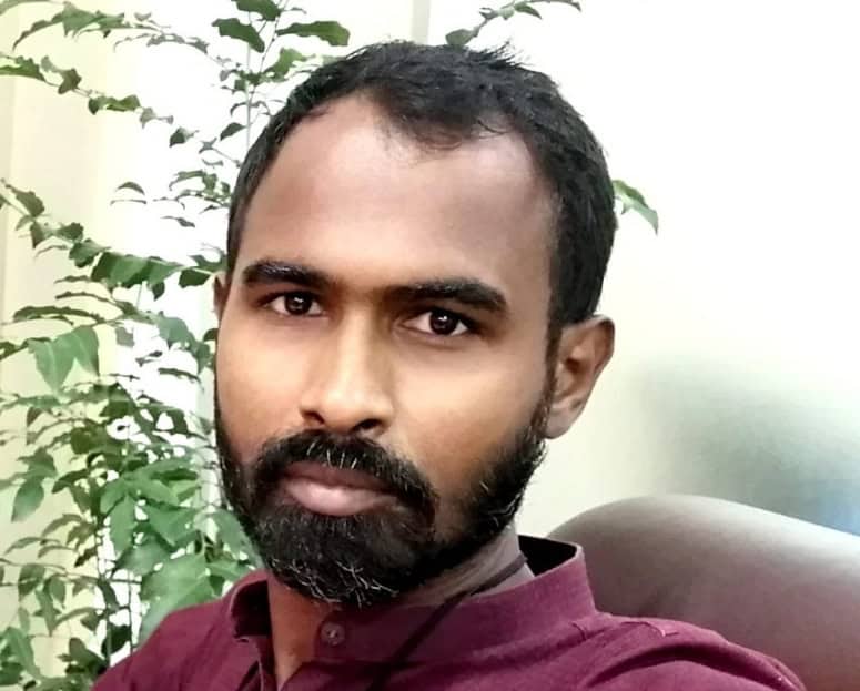 বাংলাদেশের একজন সাংবাদিকের ছবি, তিনি বসে আছেন, পেছনে গাছের পাতা. Channel i News - চ্যানেল আই নিউজ