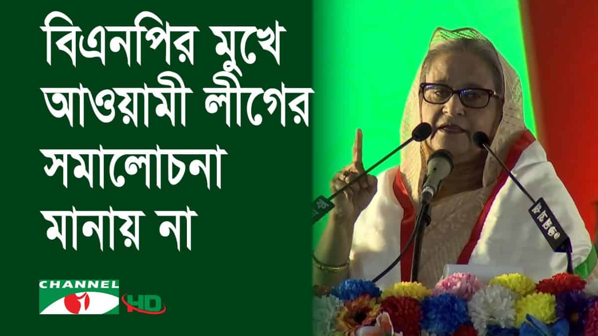 প্রধানমন্ত্রী শেখ হাসিনা ভাষণ দিচ্ছেন, পেছনে সবুজ ও লাল ব্যাকড্রপ।. Channel i News - চ্যানেল আই নিউজ