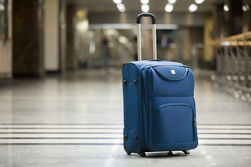 Large blue wheeled suitcase standing on the floor in modern airport terminal. Copy space