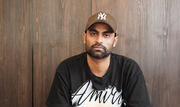Portrait of a man wearing a brown cap and black T-shirt with 'Amir' written on it. Channel i News - চ্যানেল আই নিউজ