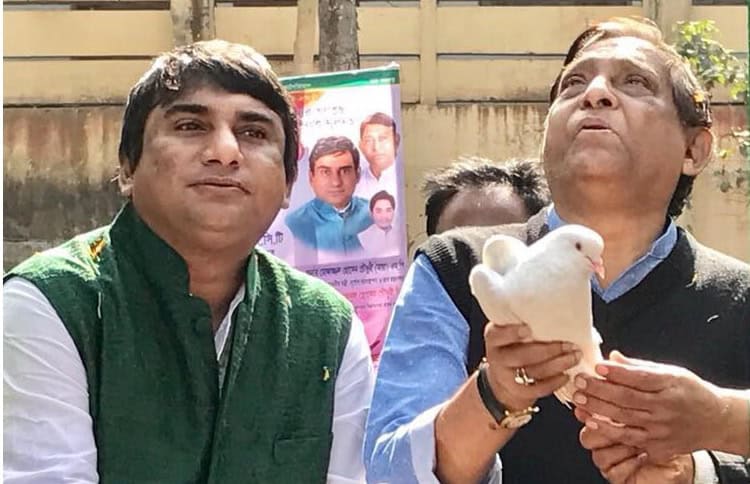 দুই ব্যক্তি, একজন পাখি পুতুল ধরে আছেন, বাইরে ছবি তোলা হচ্ছে. Channel i News - চ্যানেল আই নিউজ