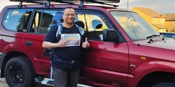 একজন ব্যক্তি গাড়ির পাশে দাঁড়িয়ে শুভেচ্ছা জানাচ্ছেন. Channel i News - চ্যানেল আই নিউজ