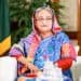 প্রধানমন্ত্রী বৈঠকে বসে আছেন, পেছনে বাংলাদেশের পতাকা দেখা যাচ্ছে।. Channel i News - চ্যানেল আই নিউজ