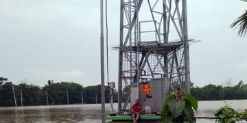 বন্যার কারণে ক্ষতিগ্রস্ত মোবাইল টাওয়ার ও একজন ব্যক্তি বসে আছেন. Channel i News - চ্যানেল আই নিউজ