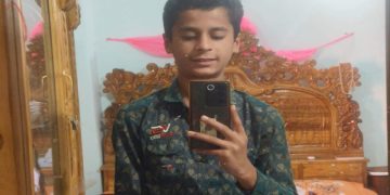 ছাত্রের ছবি, সে মোবাইল দিয়ে ছবি তুলছে, বিছানার পাশে কাঠের আসবাবপত্র. Channel i News - চ্যানেল আই নিউজ