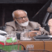 Senior man using smartphone at a meeting table with glasses of water. Channel i News - চ্যানেল আই নিউজ