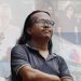 একজন ব্যক্তি চোখ বন্ধ করে দাঁড়িয়ে আছেন, পেছনে বিভিন্ন মানুষ ও স্থান দেখা যাচ্ছে. Channel i News - চ্যানেল আই নিউজ