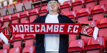 বাংলাদেশি ফুটবল প্রেমী Morecambe FC দলের স্কার্ফ ধরে দাঁড়িয়ে. Channel i News - চ্যানেল আই নিউজ