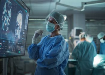 Professional Focused Caucasian Female Surgeon Reviewing Patient's Brain Scans on a Large Monitor, Preparing to Lead Her Team in a Complex Surgery, Analyzing Data Before the Procedure Begins