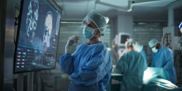 Professional Focused Caucasian Female Surgeon Reviewing Patient's Brain Scans on a Large Monitor, Preparing to Lead Her Team in a Complex Surgery, Analyzing Data Before the Procedure Begins